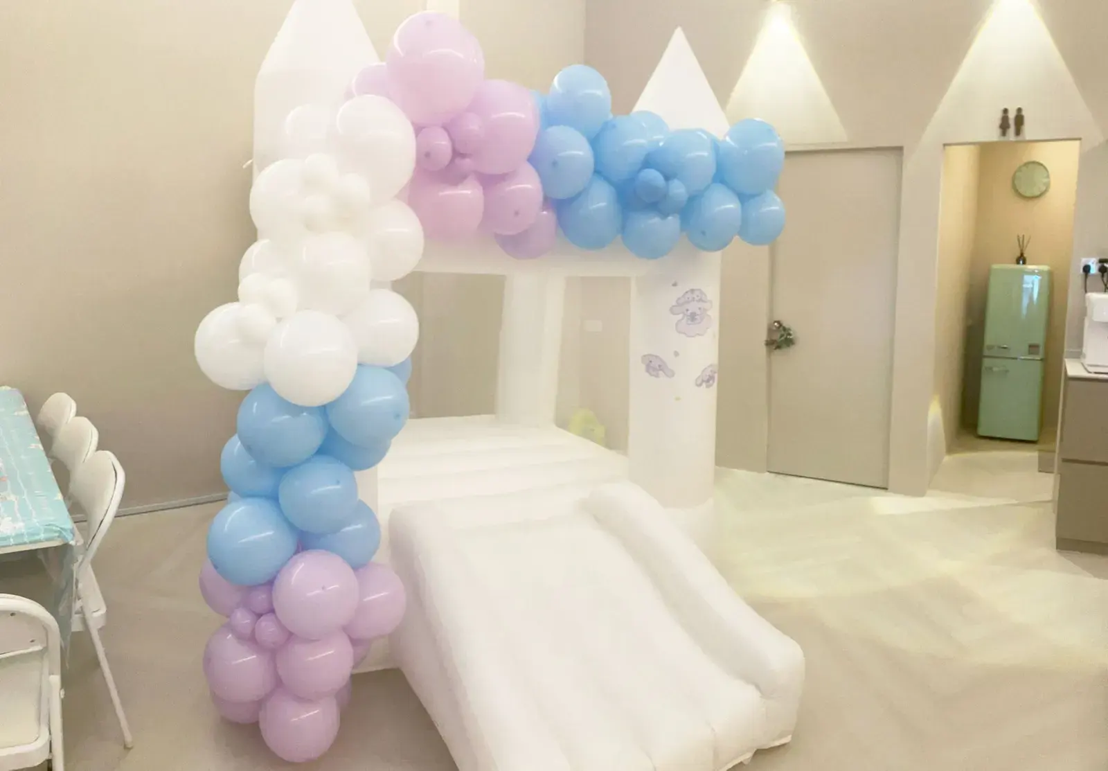 A pastel balloon arch beside a white bouncy castle with a slide